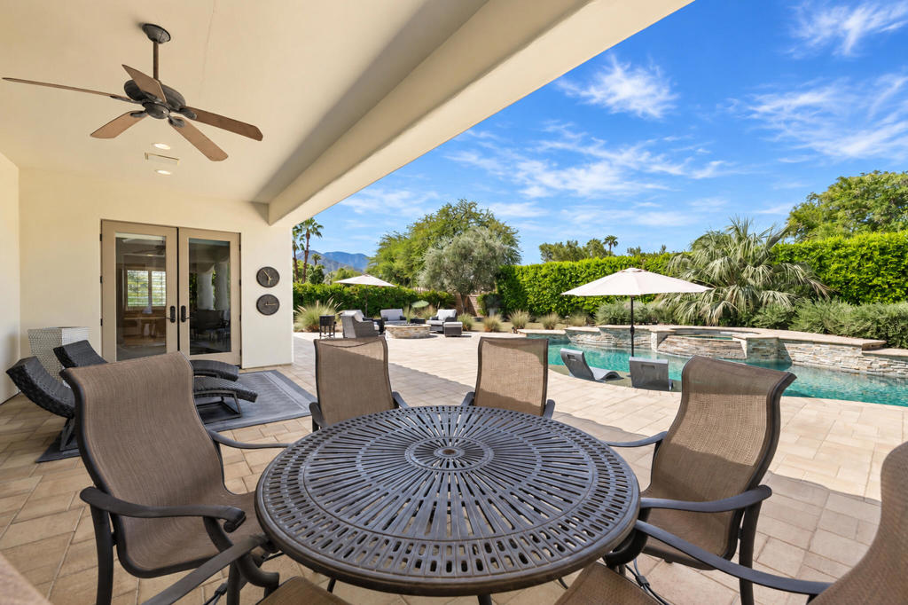 Covered patio with round dining table overlooking a landscaped swimming pool and distant mountains.