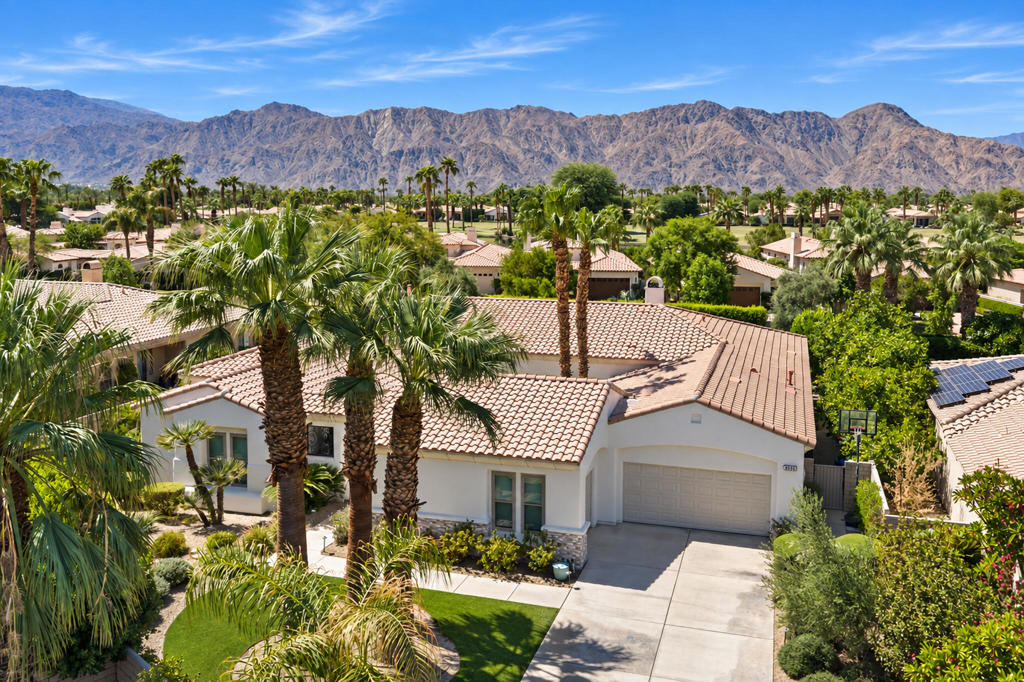 Aerial view of a stucco home with a tiled roof, palm trees, and mountain backdrop.