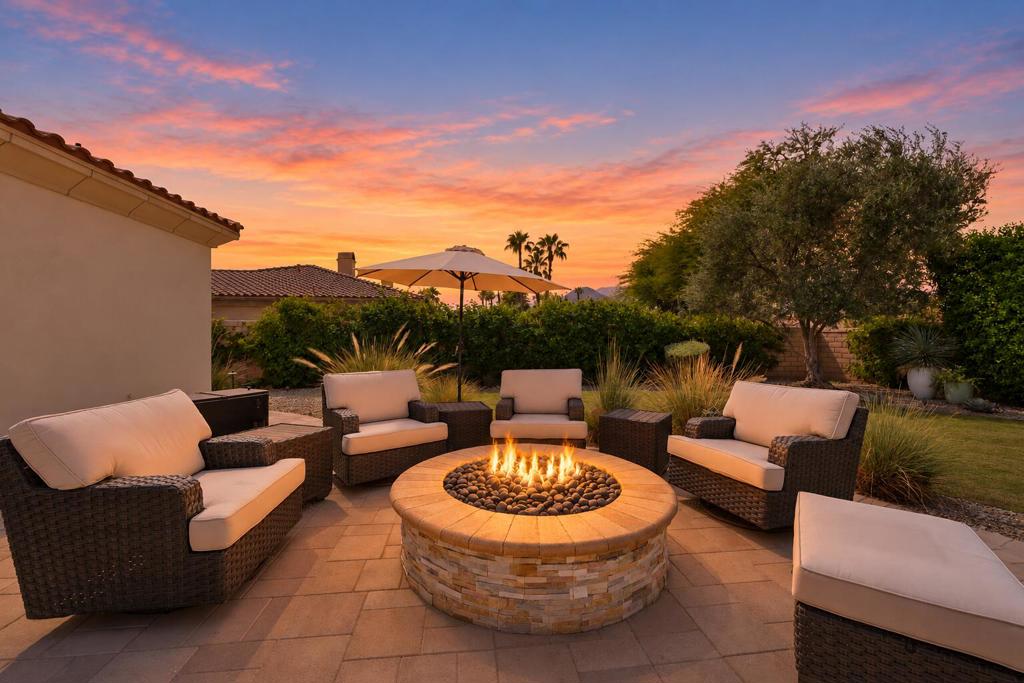 Outdoor patio with cushioned wicker seating around a lit stone fire pit at sunset.