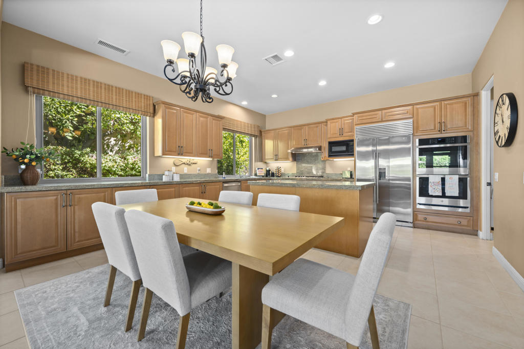 Kitchen and dining area with wood cabinetry, stainless steel appliances, and a large table beside garden-facing windows.