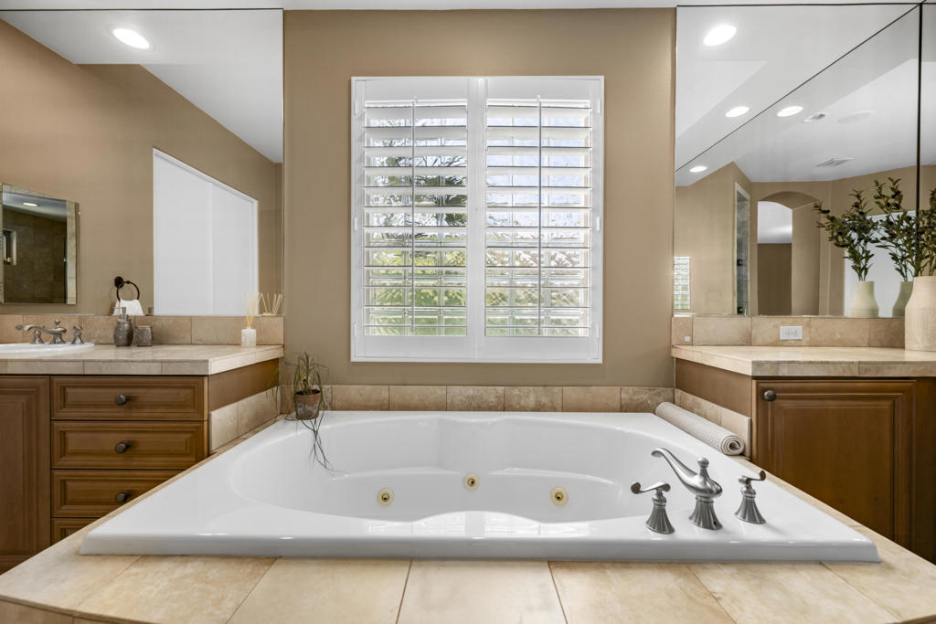 Bathroom with a large jetted tub, mirrored vanities, and plantation shutters.