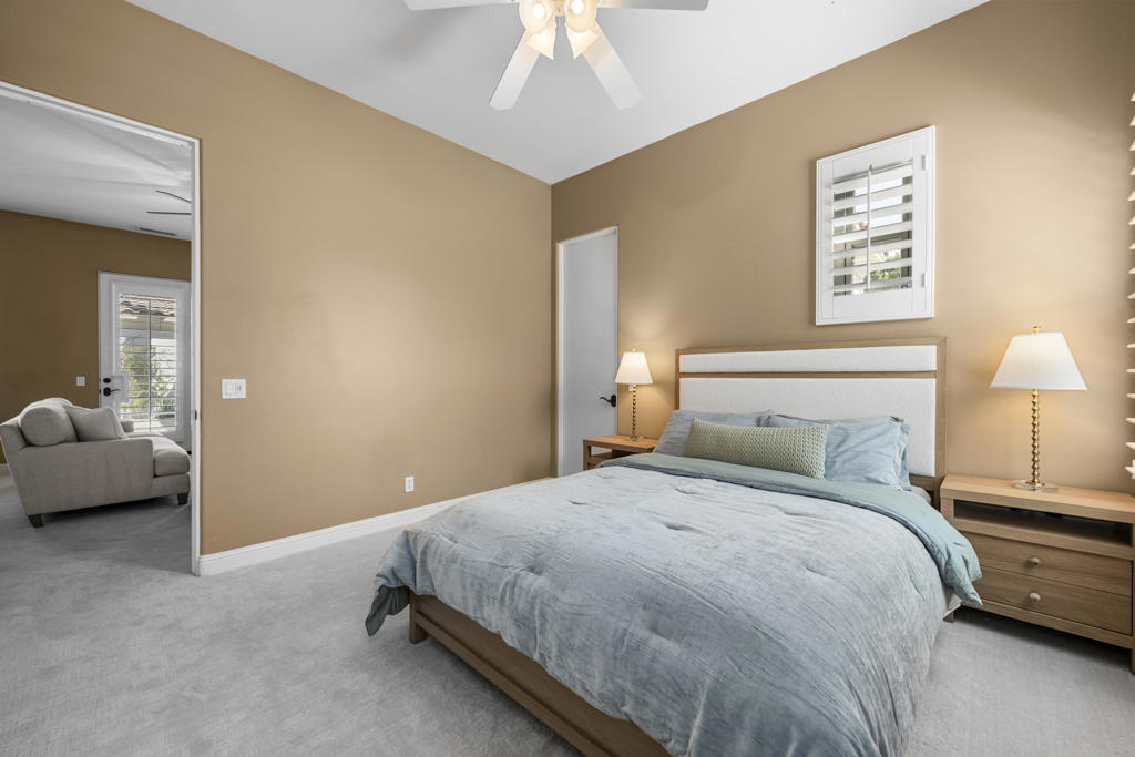 Staged bedroom with a king bed, tan walls, and a sitting area visible through the doorway.