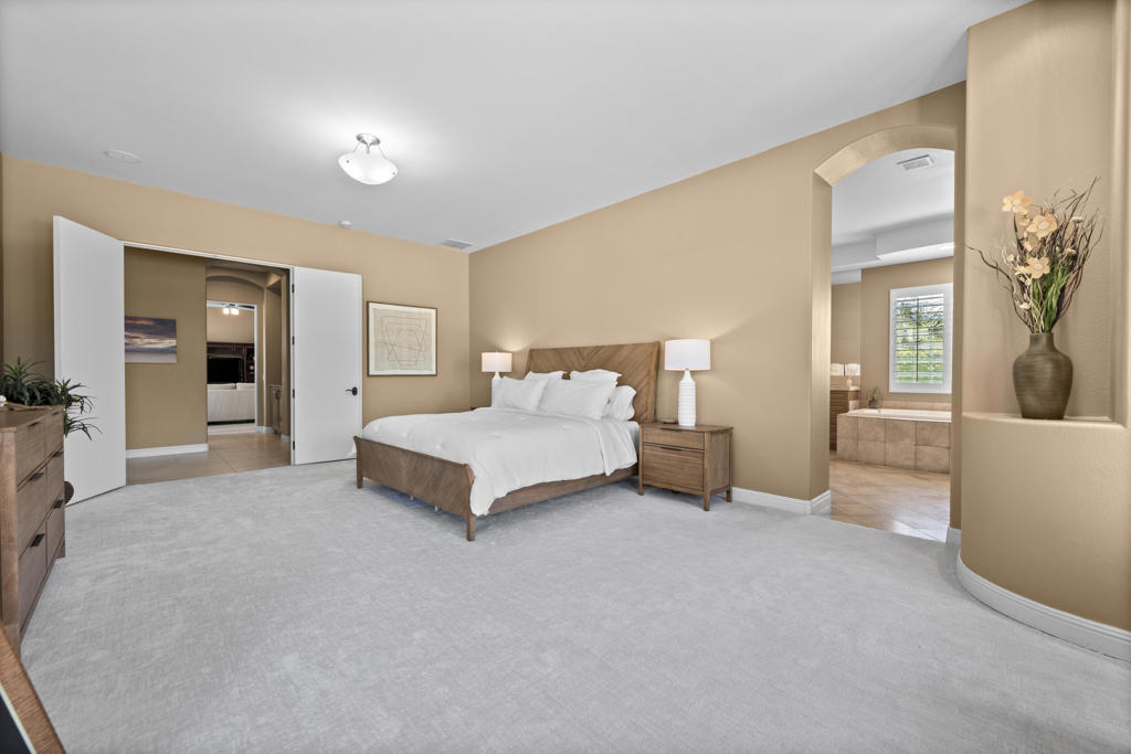 Primary bedroom with a wood-frame bed, neutral carpeting, and an arched opening to the bathroom.