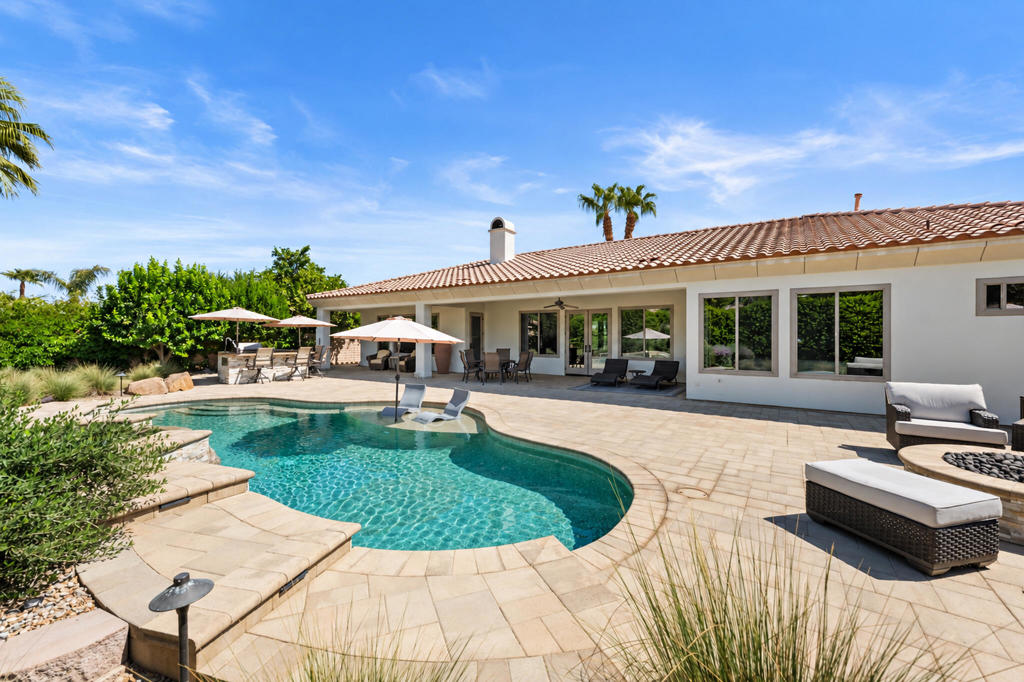 Backyard pool and patio beside a single-story home with a tile roof.