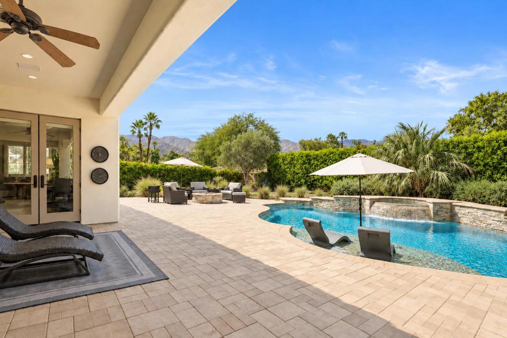 Backyard pool and paved patio with lounge chairs, umbrellas, and mountain views.