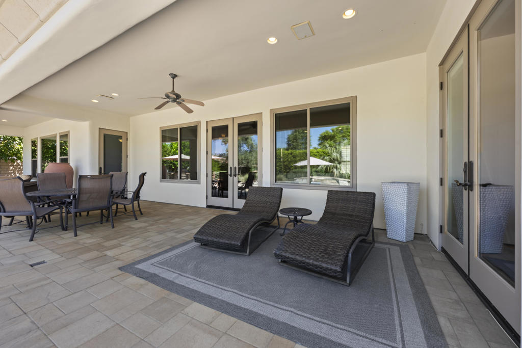 Covered patio with two chaise lounges, a dining set, and glass doors overlooking the garden.