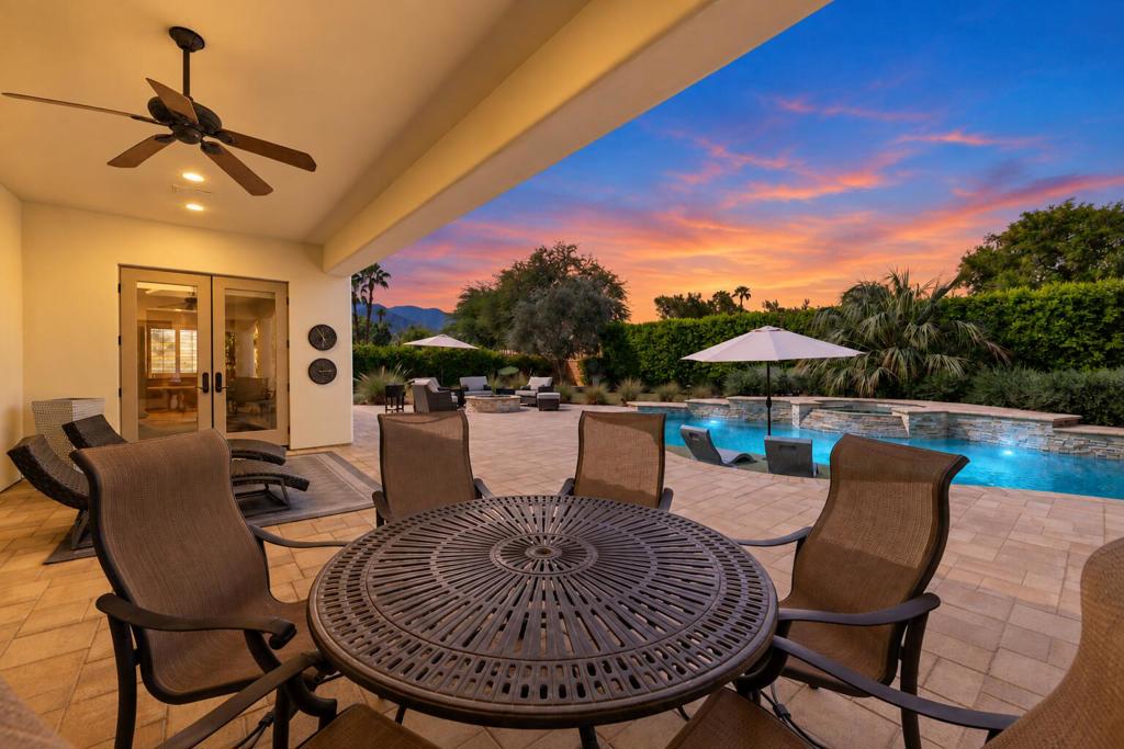 Covered patio with outdoor dining furniture overlooking a swimming pool at sunset.