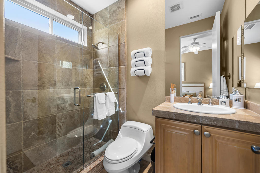Bathroom with a glass-enclosed stone-tile shower, white toilet, and wood vanity.