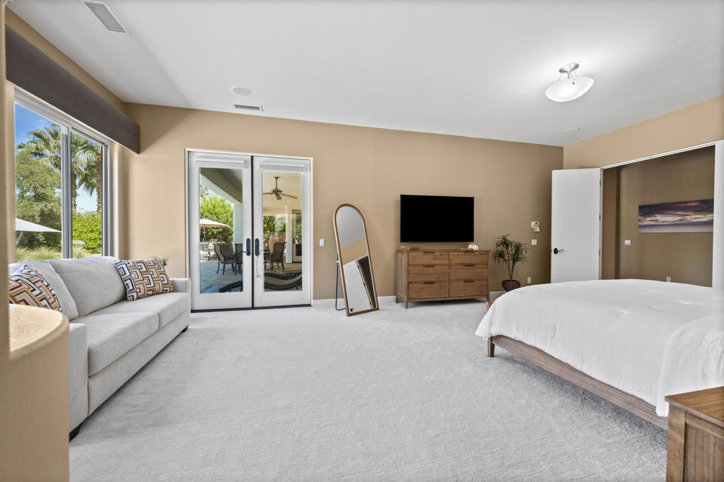 Bright bedroom with a white bed, gray sofa, and sliding glass doors opening to a patio.
