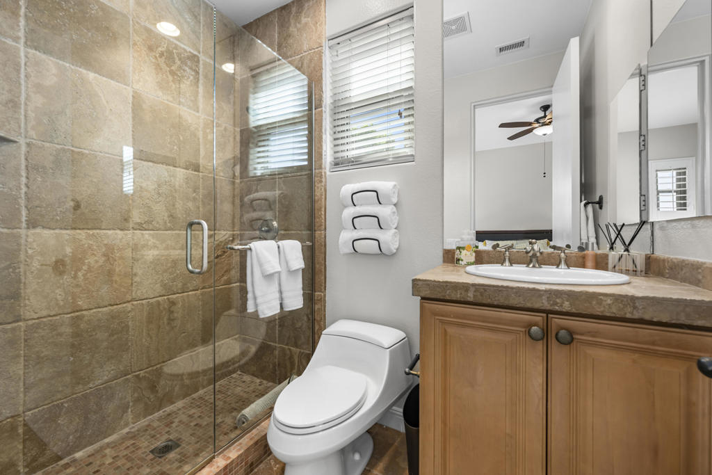 Bathroom with a glass-enclosed stone-tile shower and a wood vanity.