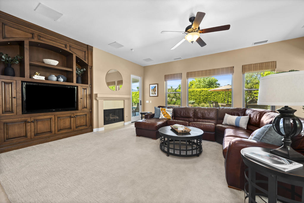 Living room with a built-in wood entertainment center, fireplace, leather sectional, and garden-facing windows.