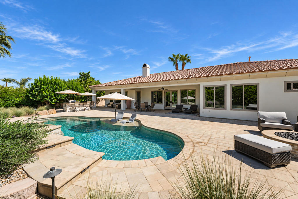 Backyard pool and paved patio with lounge seating beside a single-story home.