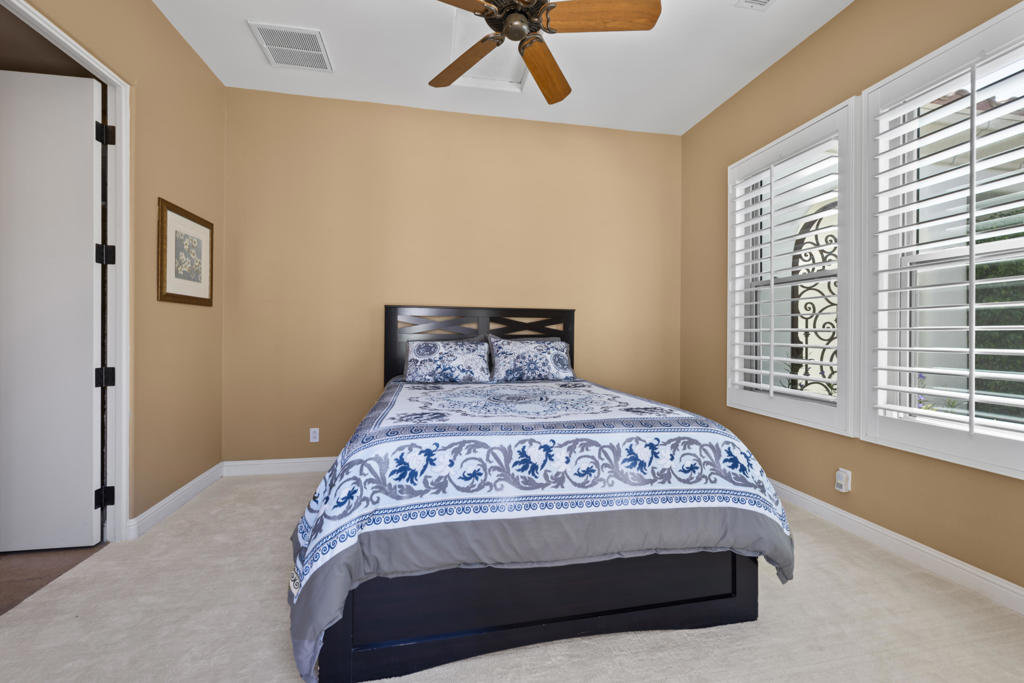 Bedroom with a patterned bed, tan walls, and plantation shutters.