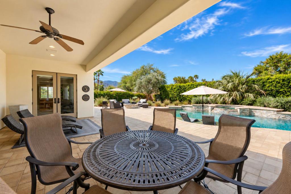 Covered patio with a round dining table overlooks a swimming pool and mountain views.