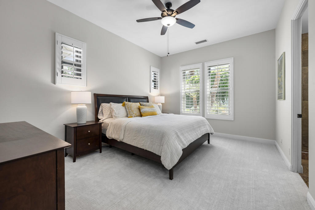 Bedroom with a dark wood bed, white bedding, plantation shutters, and a ceiling fan.