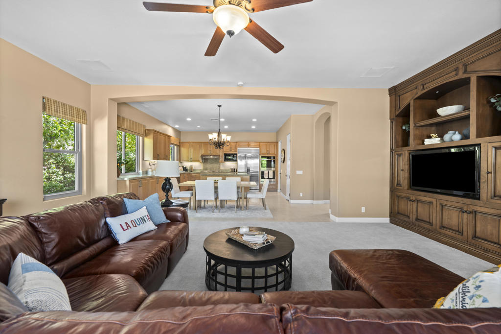 Furnished living room with leather seating, built-in entertainment center, and open kitchen beyond.