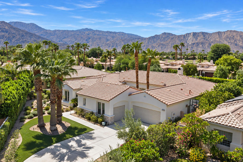 Desert home with a tile roof, palm-lined lawn, and mountains in the background