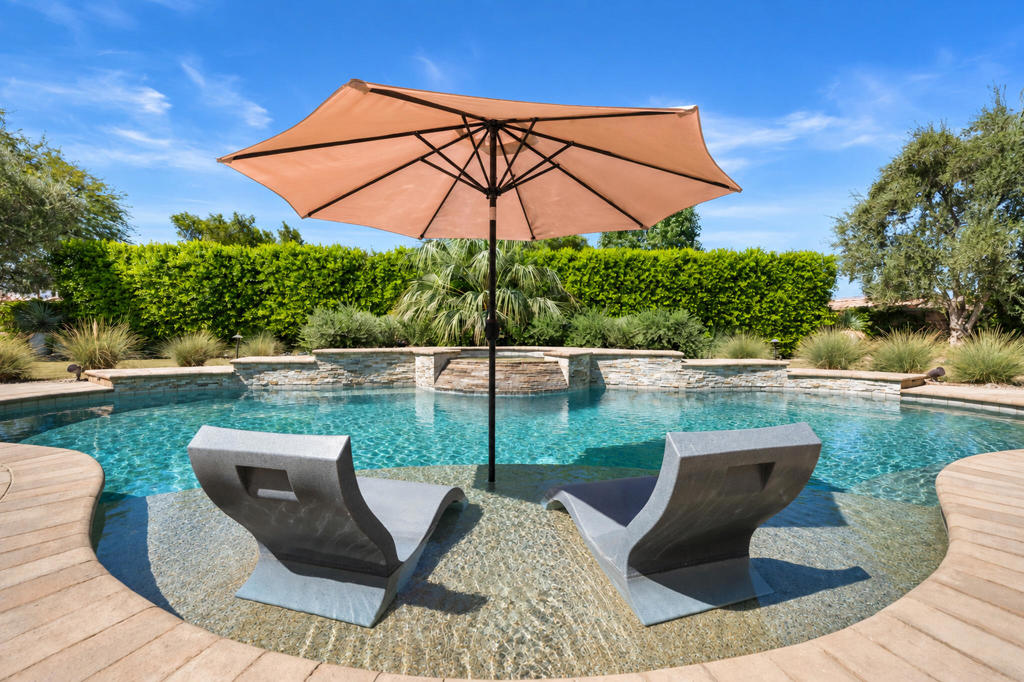 Pool with a shallow sun shelf, two lounge chairs, and a large tan umbrella.