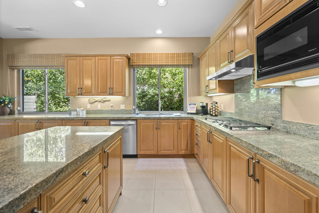 Kitchen with warm wood cabinets, granite countertops, a central island, and windows overlooking greenery.