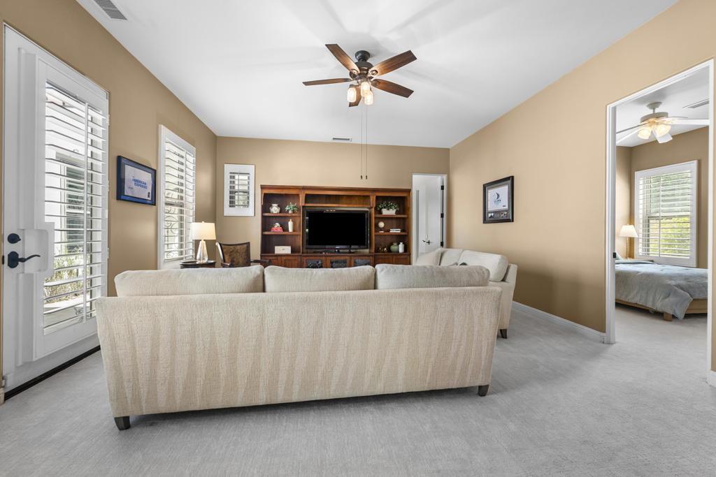 Living room with beige walls, a large wooden entertainment center, and plantation-shuttered windows.