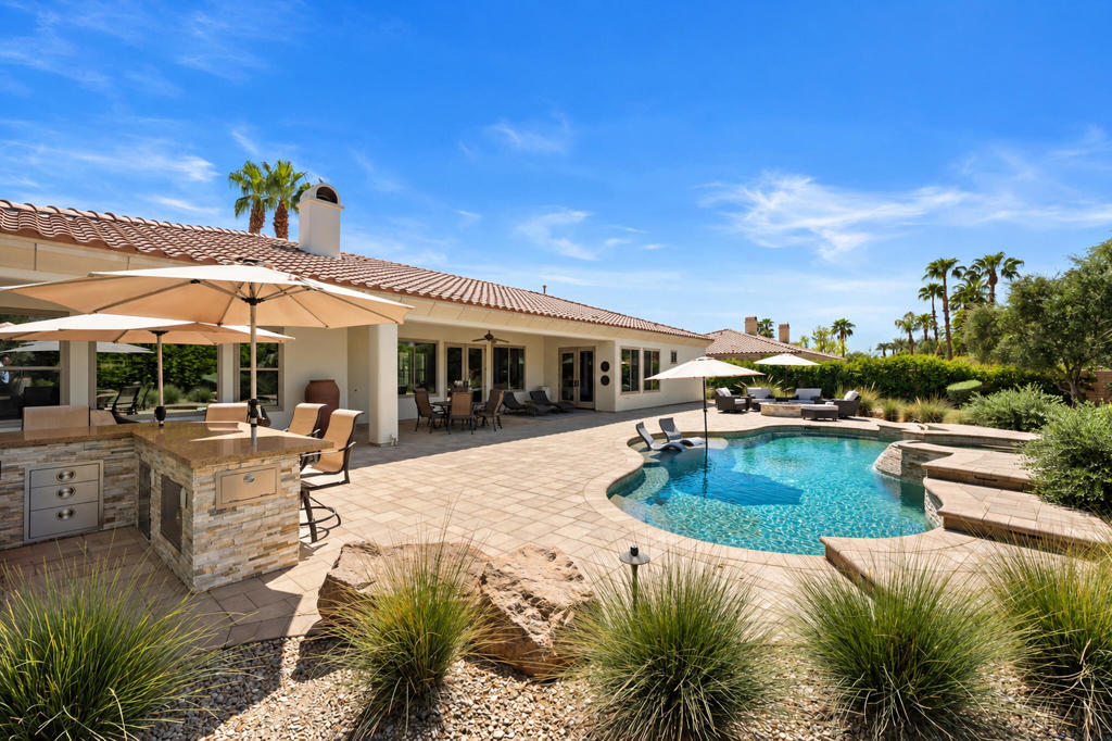 Backyard with a curved swimming pool, stone patio, outdoor kitchen, and desert landscaping.