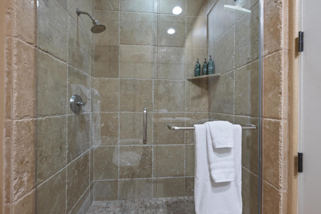 Walk-in shower with tan stone tile, glass doors, and a towel bar.