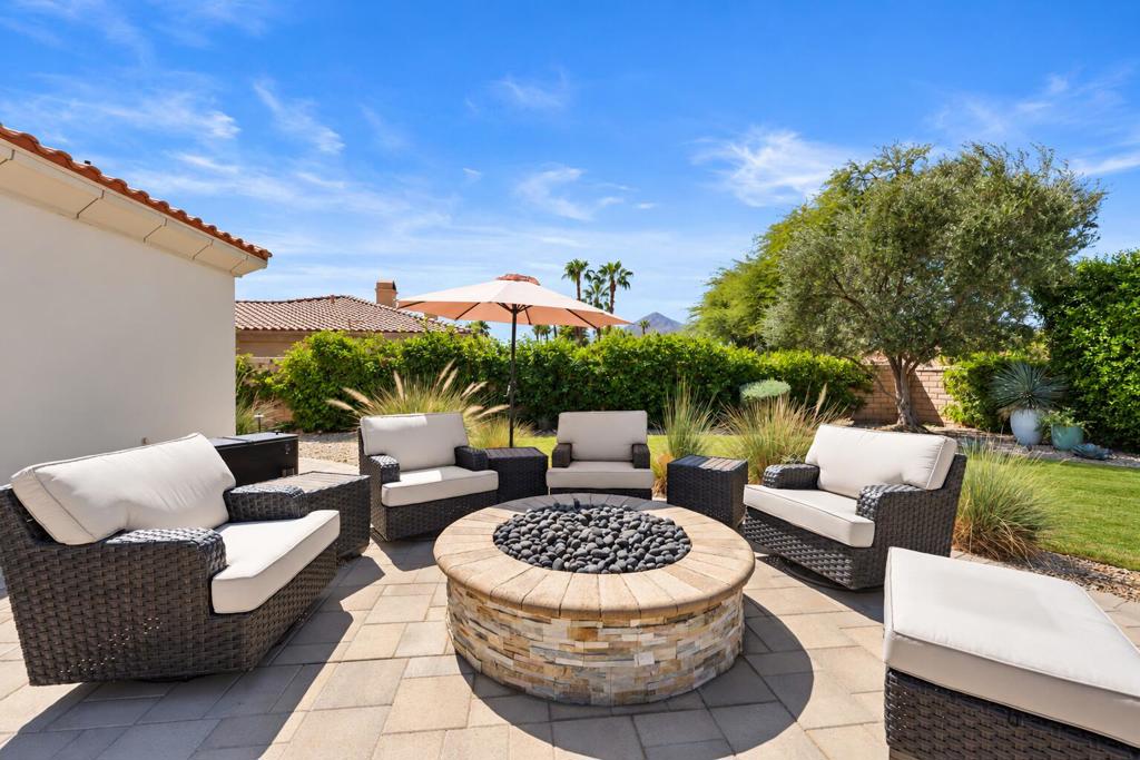 Backyard patio with cushioned wicker seating around a stone fire pit, beside a landscaped lawn.