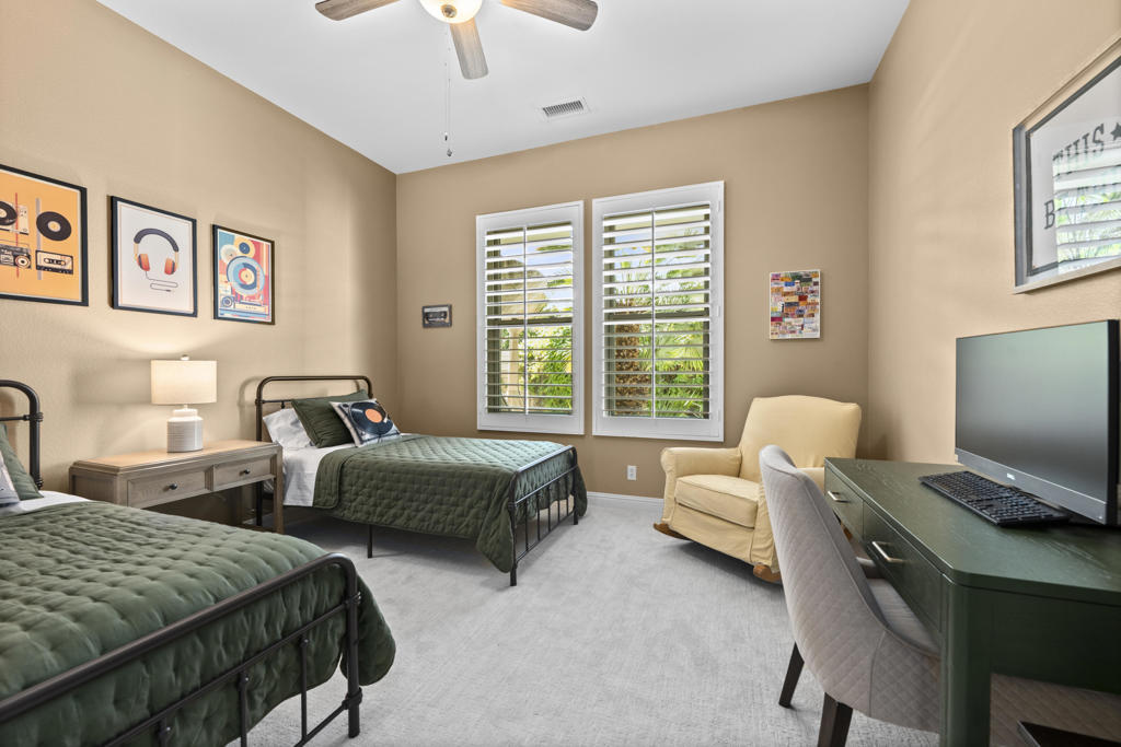 Bedroom with two green-covered beds, plantation shutters, and a desk with a computer.