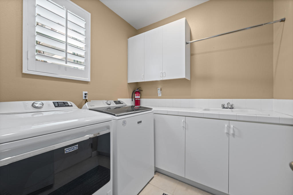 Laundry room with front-loading washer and dryer, white cabinets, and a utility sink.