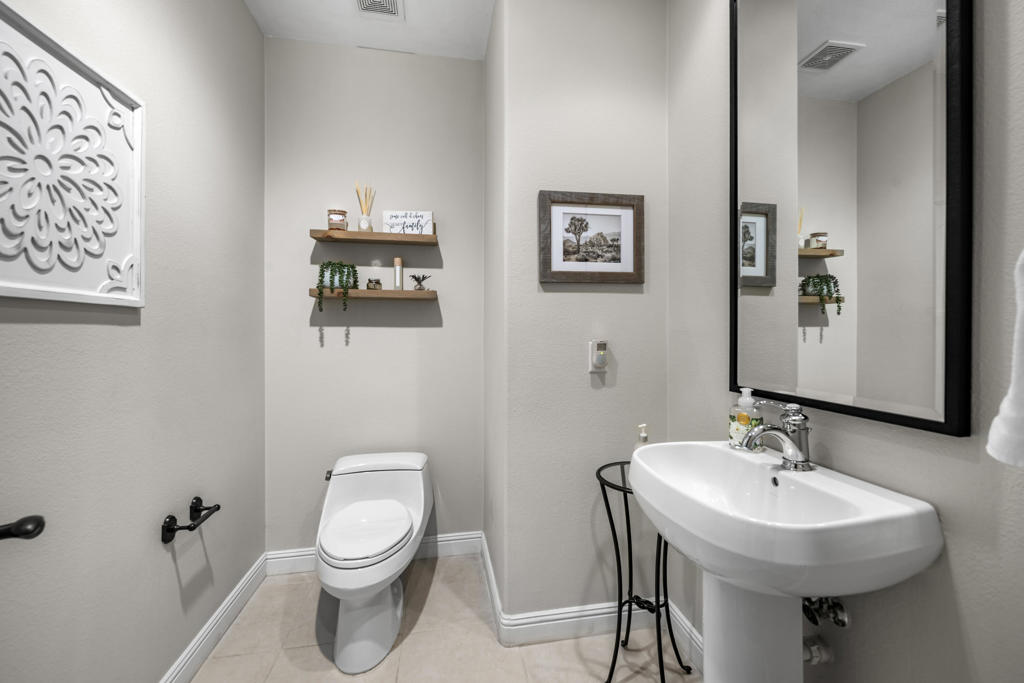 Bathroom with a pedestal sink, toilet, large mirror, and floating wooden shelves.