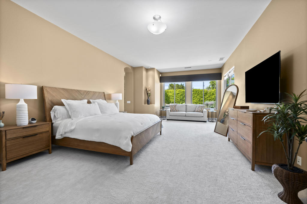 Primary bedroom with a king bed, sitting area, and large windows overlooking greenery.