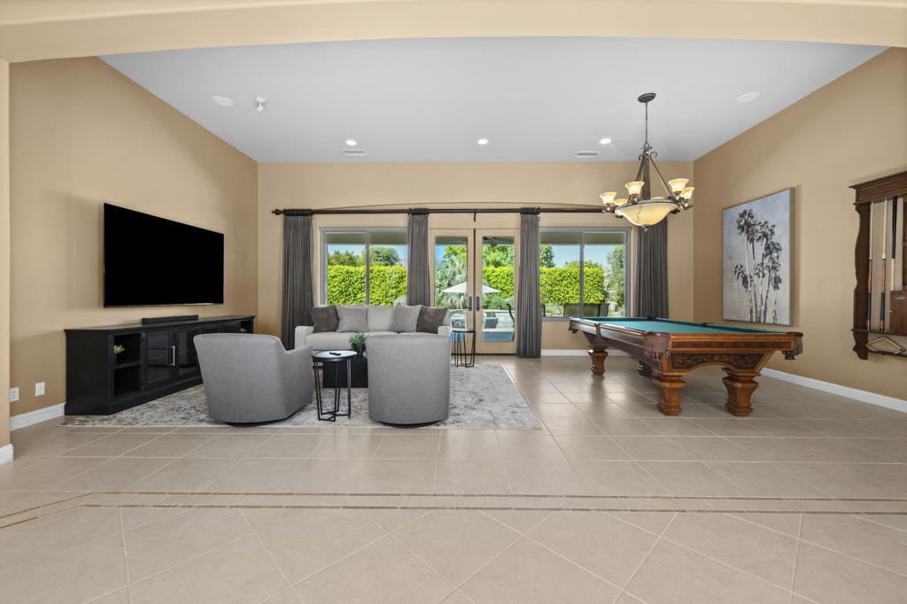 Game room with a pool table, gray seating, and wide windows overlooking a green hedge.