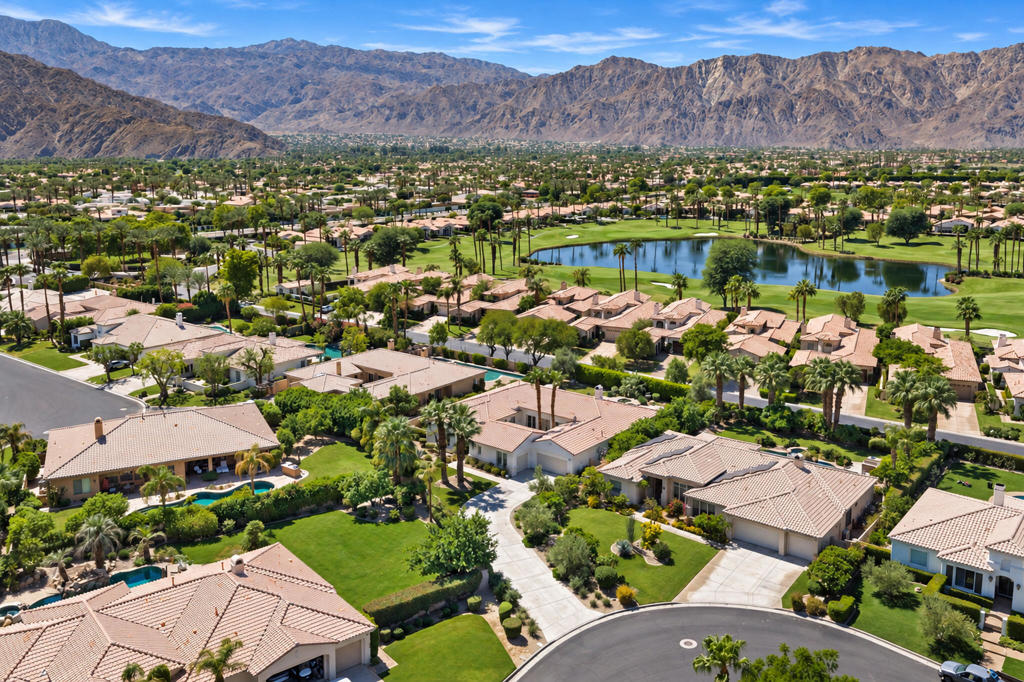 Aerial view of La Quinta homes beside a golf course pond, with desert mountains beyond.