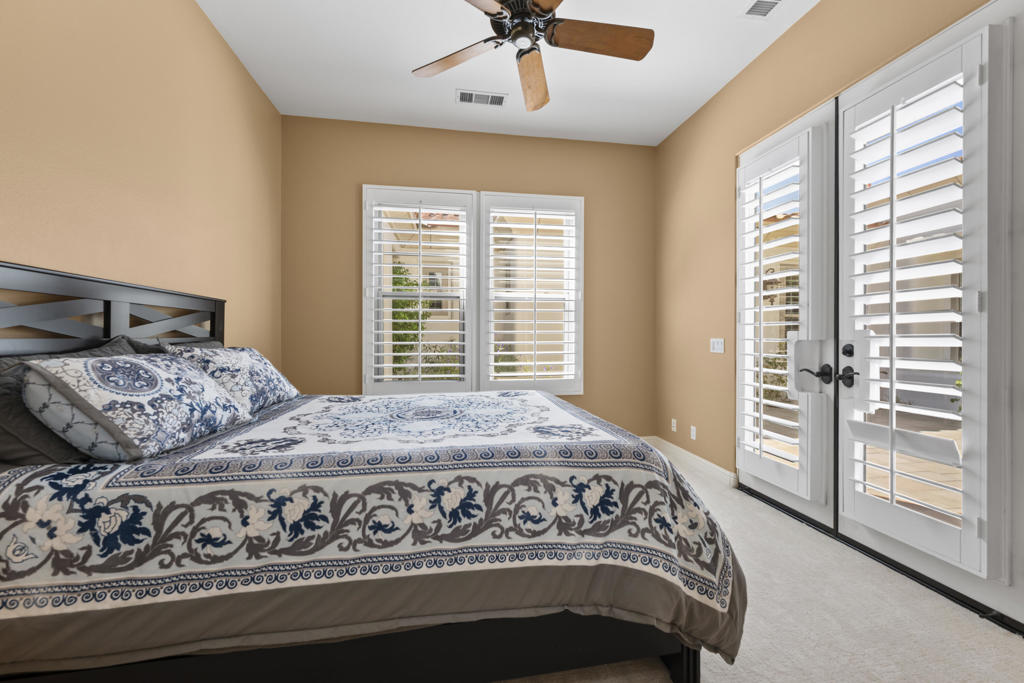 Bedroom with a patterned bed, plantation shutters, and glass doors opening to a patio.