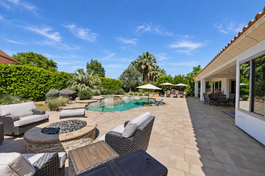 Backyard pool and stone patio with wicker lounge seating beside a covered outdoor dining area.