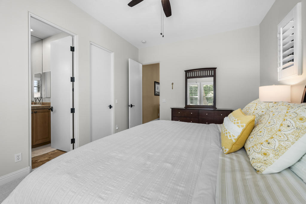 Bedroom with a white bed, yellow accent pillow, dark wood dresser, and an open bathroom doorway.