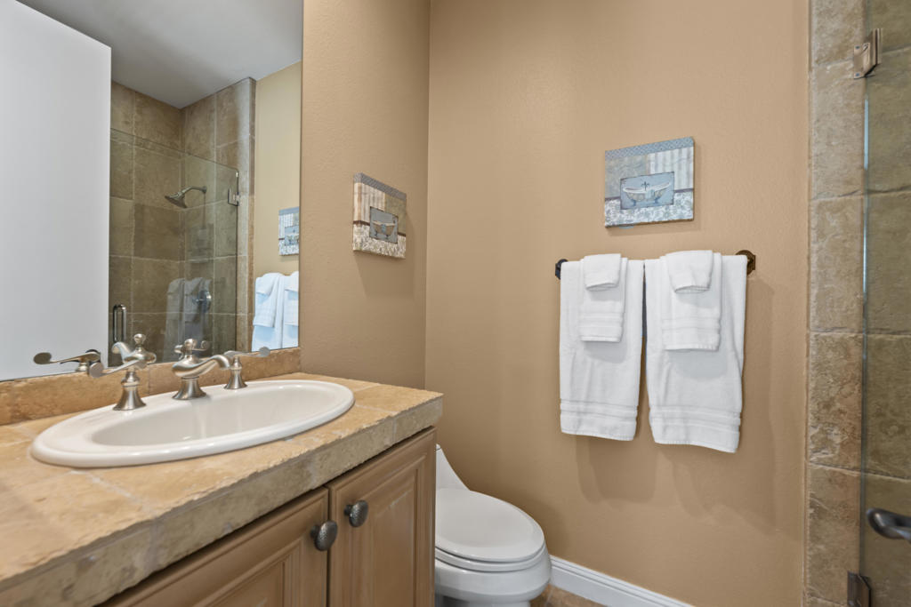 Bathroom with a stone countertop vanity, toilet, and glass-enclosed tiled shower.