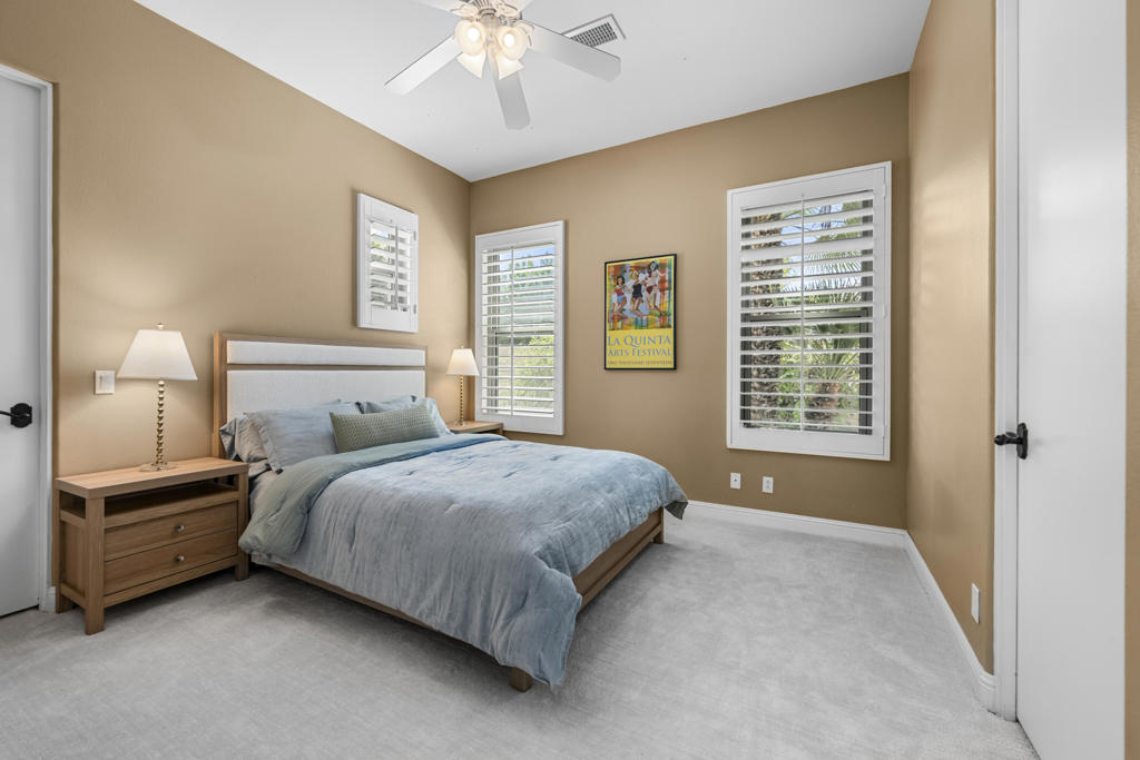 Bedroom with a king bed, wood nightstands, plantation shutters, and tan walls.