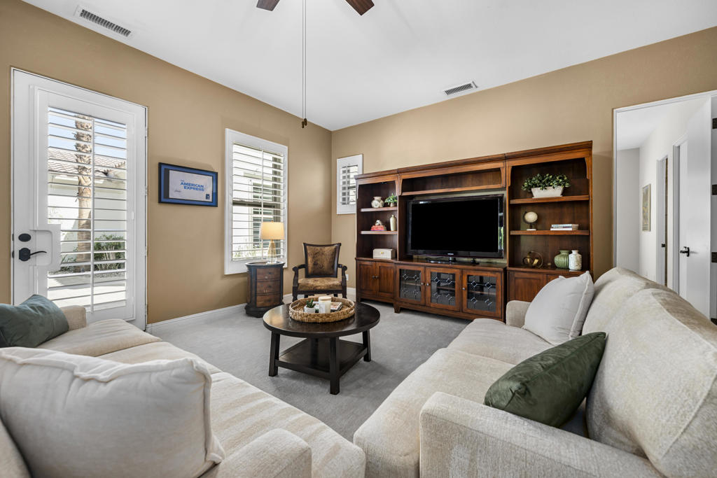 Living room with cream sofas, a dark wood entertainment center, and plantation shutters.