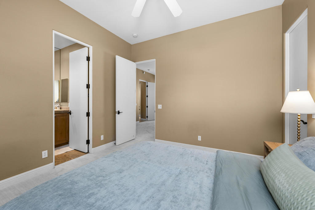 Bedroom with tan walls, pale blue carpet, and doors opening to a bathroom and hallway.