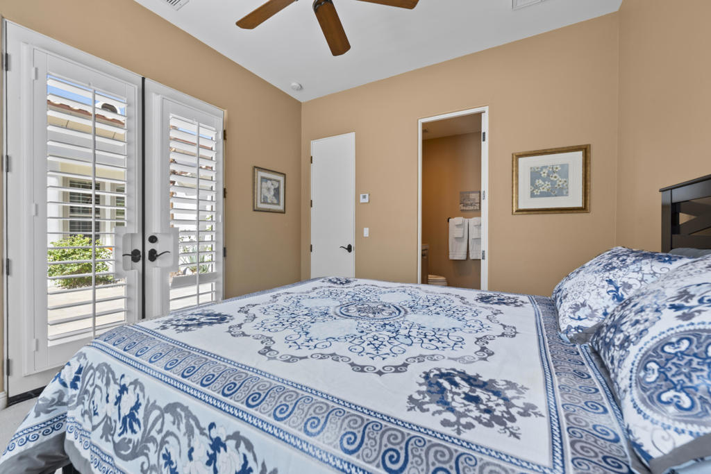 Bedroom with a blue-and-white patterned bedspread, plantation shutters, and an open bathroom doorway.