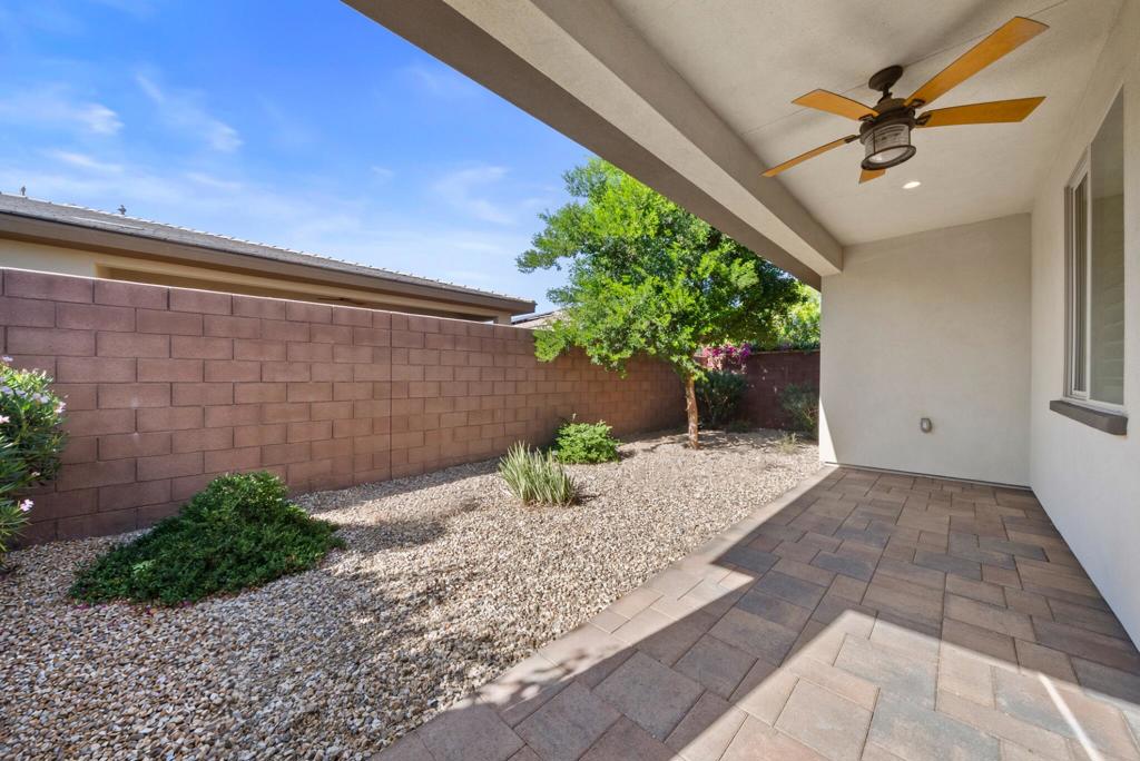 Covered patio with paver flooring, ceiling fan, and a gravel yard enclosed by a block wall.