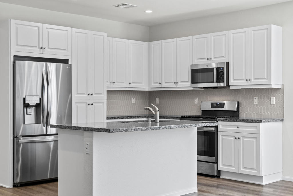 Kitchen with white cabinets, stainless steel appliances, patterned backsplash, and a granite-topped island.