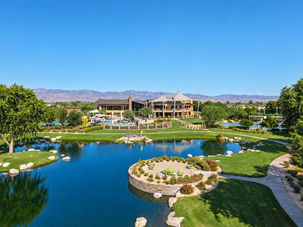 Community clubhouse and pool beyond a landscaped pond, with mountains in the distance.
