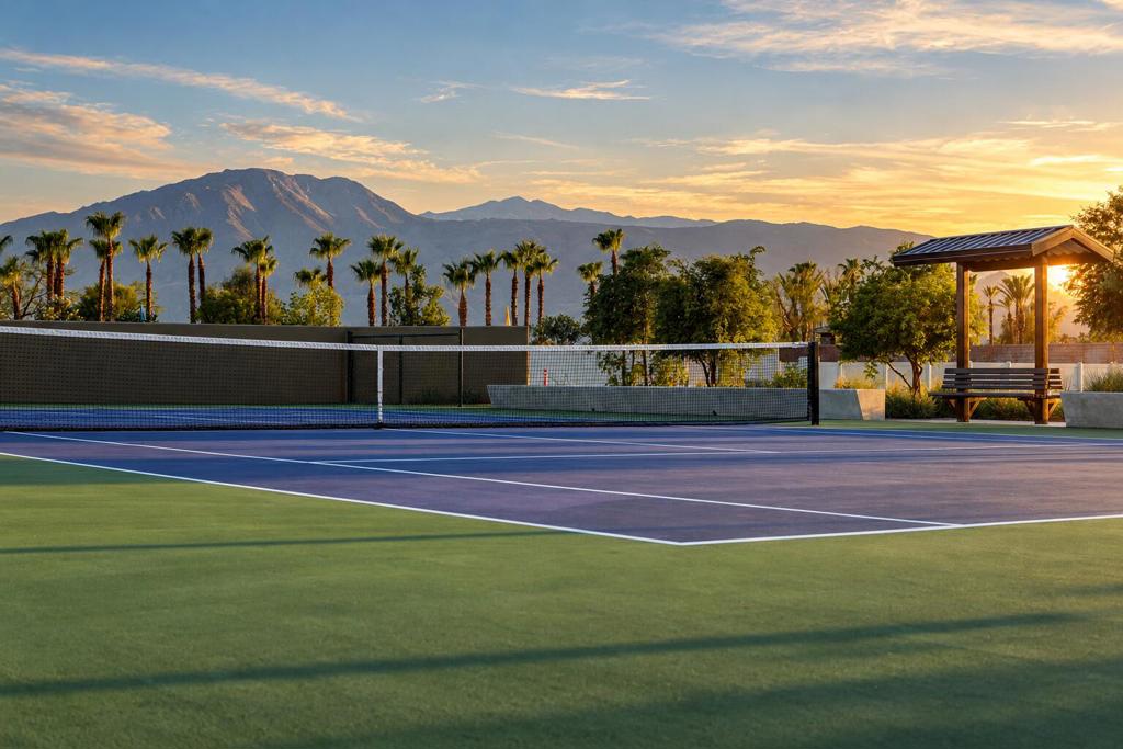 Tennis court with mountain views, palm trees, and a shaded pavilion at sunset.