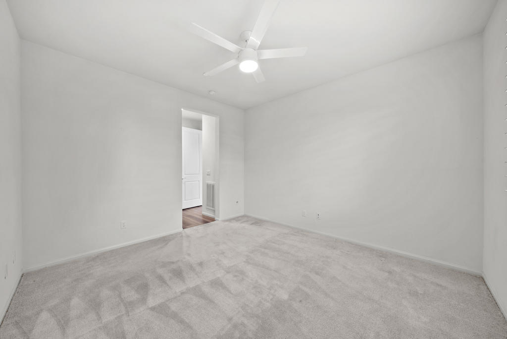 Empty carpeted bedroom with a white ceiling fan and open doorway.