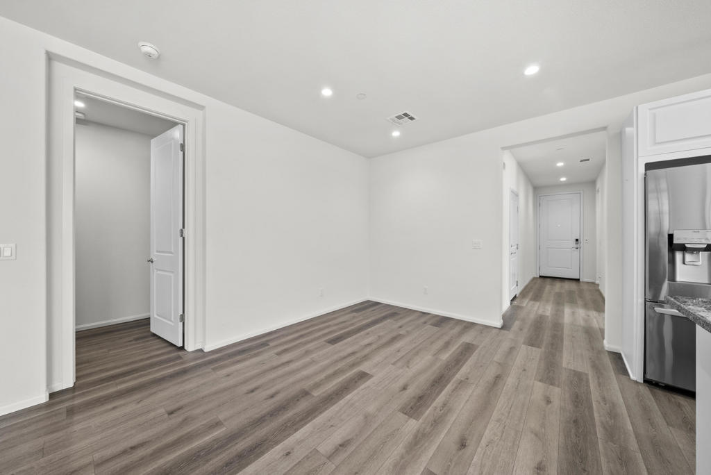 Vacant interior with wood-look flooring, a hallway, and part of the kitchen.