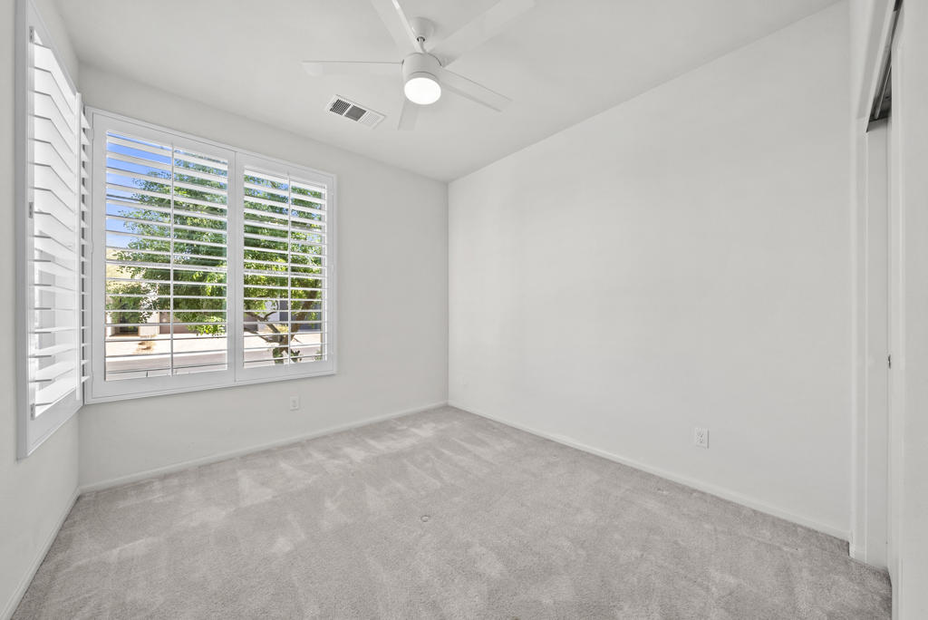 Empty carpeted room with plantation shutters and a ceiling fan.