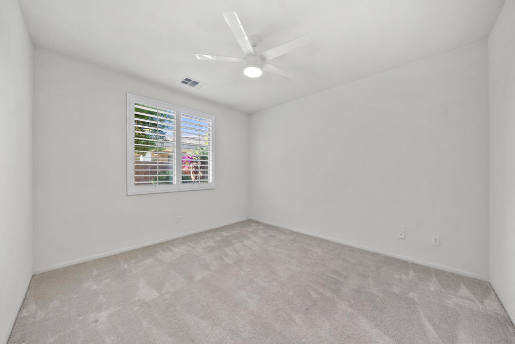 Empty carpeted room with a shuttered window and ceiling fan.
