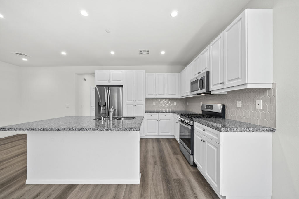 Kitchen with a granite island, white cabinets, stainless steel appliances, and wood-look flooring.